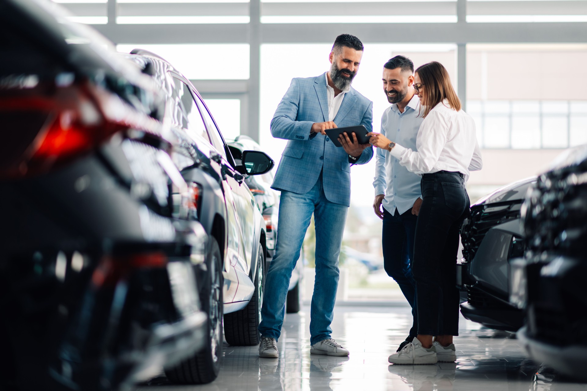 Car dealership trio assessing vehicle options with tablet view